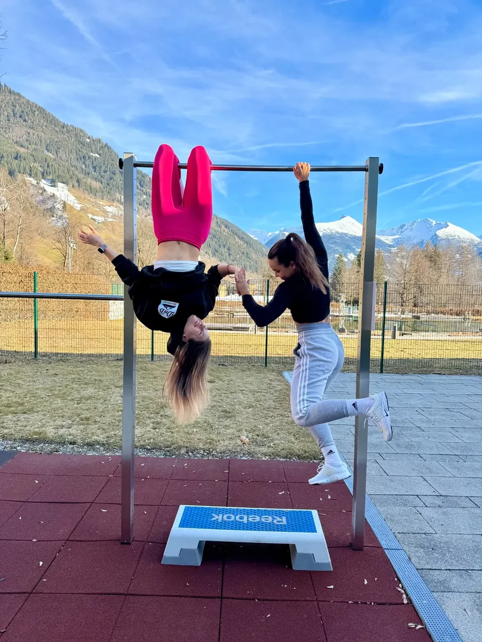 Dóri and Bogi having fun on outdoor exercise bars with mountains behind them