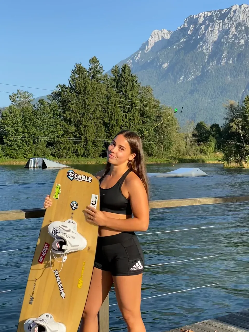 Bogi holding her wakeboard beside an alpine lake